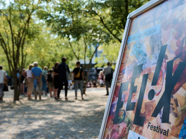 Ein Schild mit der Aufschrift »FELIX Festival« steht im Vordergrund, während Menschen im Hintergrund schlendern.