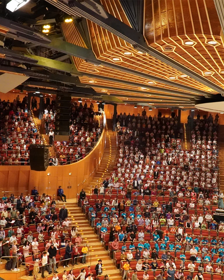 Kölner Philharmonie: Ein großes Auditorium voller Menschen in farbenfroher Kleidung während einer Veranstaltung. Die Architektur ist modern und stilvoll gestaltet.