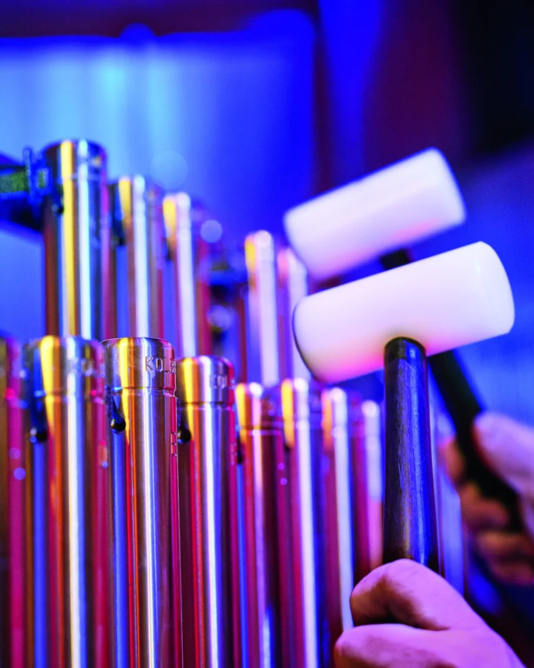 Nahaufnahme eines musikalischen Instruments mit Metallröhren. Zwei Hände halten Schlägel und schlagen auf die Röhren. Bunte Beleuchtung.