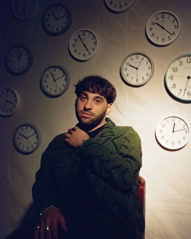 Samora Pinderhughes is sitting in front of a wall full of clocks.