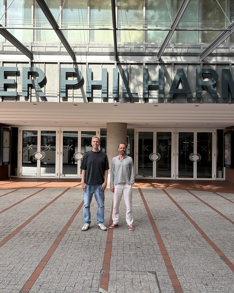 Zwei Personen (Daniel Danger und Thomas Posth) stehen vor dem Eingang der Kölner Philharmonie, einem bekannten Veranstaltungsort für klassische Musik in Deutschland.