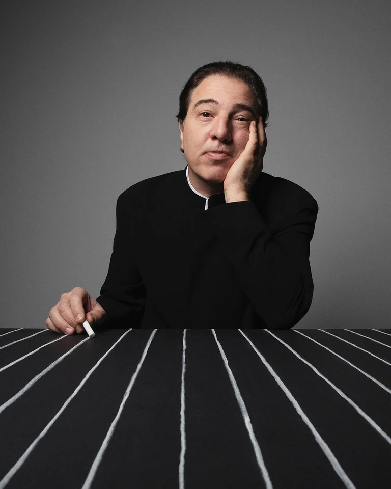 Eine Person in einem schwarzen Anzug (Fazıl Say) sitzt an einem Tisch mit weißen Linien, in einen nachdenklichen Ausdruck vertieft.