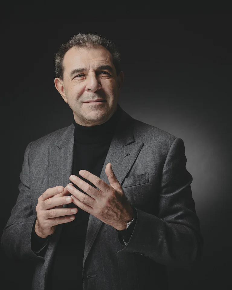 Ein Mann (Daniele Gatti) im Anzug steht vor einem dunklen Hintergrund. Er hält die Hände zueinander und blickt freundlich in die Kamera.